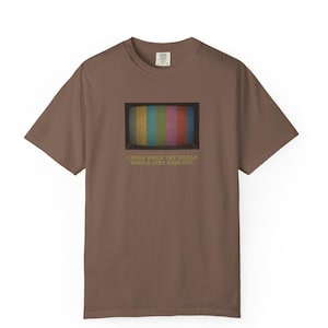 May include: Brown t-shirt featuring a retro television screen graphic with colorful bars. The text below the screen reads, "I MISS WHEN THE WORLD WOULD JUST SIGN OFF."