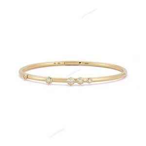May include: A delicate gold bangle bracelet featuring five round, clear gemstones. The bracelet has a simple, elegant design with a clasp closure. The gemstones are evenly spaced along the front of the bracelet.