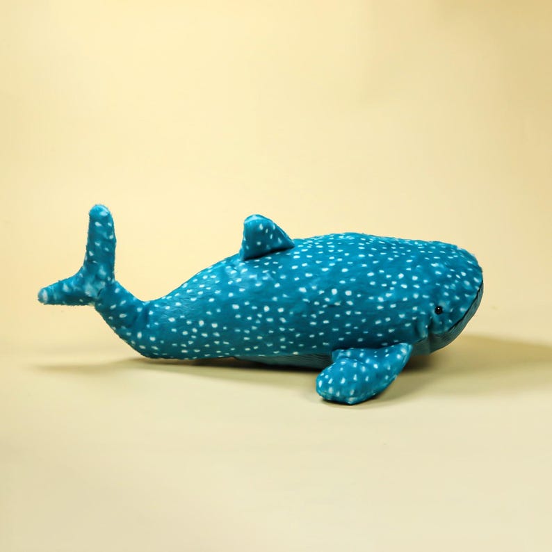 Puede incluir: Un peluche de tibur&oacute;n ballena turquesa con manchas blancas. El peluche tiene una aleta caudal, una aleta dorsal y aletas pectorales. El juguete est&aacute; hecho de material suave y est&aacute; dise&ntilde;ado para parecerse a un tibur&oacute;n ballena.