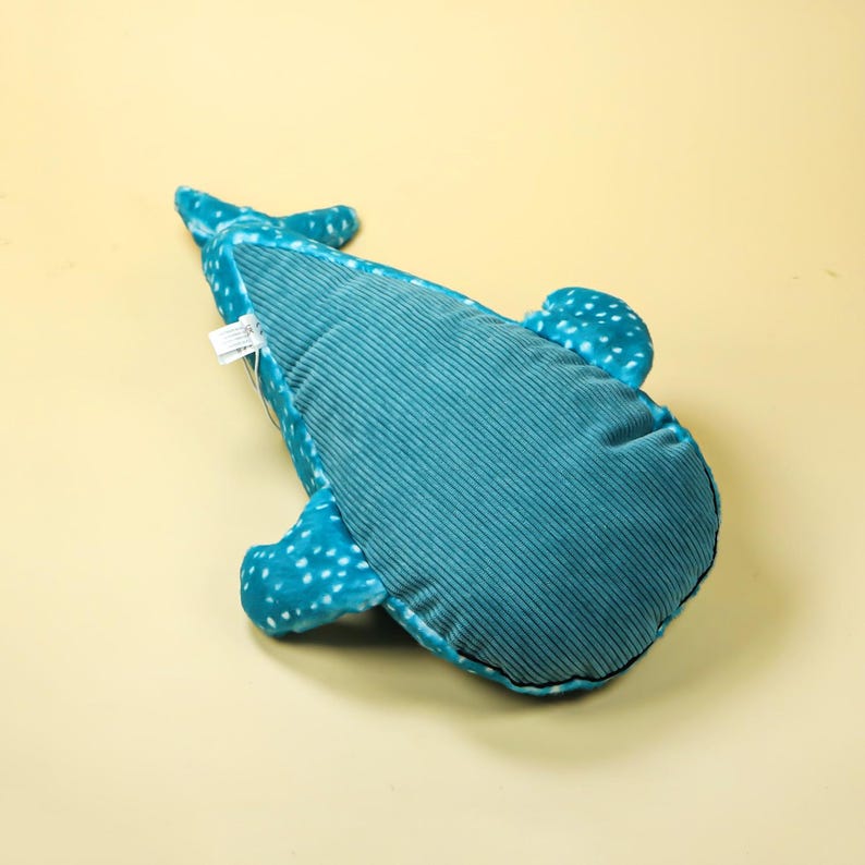Puede incluir: Un peluche de tibur&oacute;n ballena azul y turquesa. El juguete presenta lunares blancos en las aletas y una textura de pana en el cuerpo. Se encuentra sobre un fondo amarillo claro.
