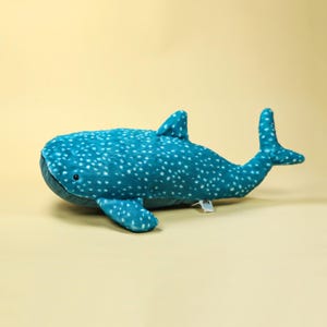 Puede incluir: Un peluche de tibur&oacute;n ballena en tonos turquesa y blanco. El juguete de peluche presenta un cuerpo texturizado con manchas blancas, aletas y cola. El juguete mide aproximadamente 70 cm de largo y representa un tibur&oacute;n ballena.