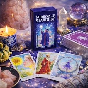 May include: A navy blue tarot card box with the text "MIRROR OF STARDUST" and an illustration of a wizard. Three tarot cards are displayed, along with a stack of cards, crystals, and a lit candle.