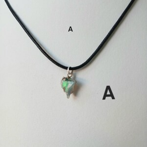 May include: A pendant necklace featuring a raw, iridescent gemstone pendant suspended from a black cord. The gemstone displays shades of green and white. The necklace is displayed against a plain white background.