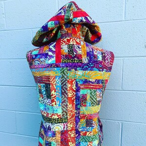 May include: A sleeveless hooded vest made from colorful patchwork fabric. The fabric is a mix of red, orange, yellow, green, blue, purple, and brown. The vest has a hood and a zipper closure.