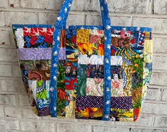 May include: A large patchwork tote bag with blue straps. The bag is made of various colorful fabrics with different patterns, including floral, geometric, and animal prints.