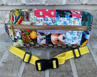 May include: A colorful patchwork fanny pack with a zipper closure and a yellow adjustable strap. The fabric features a variety of patterns, including floral, animal print, and geometric designs.