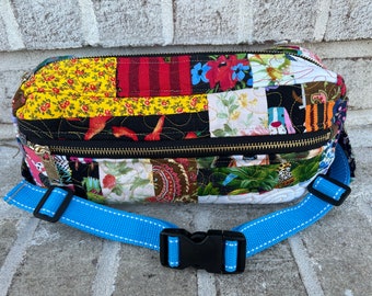 May include: A patchwork fabric fanny pack with a blue adjustable strap and a gold zipper. The fabric is a mix of floral, geometric, and animal prints.