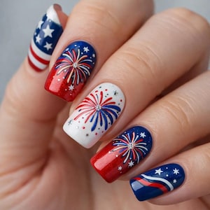May include: A hand with a manicure featuring patriotic nail art. The nails are painted in red, white, and blue with designs of fireworks, stars, and stripes. The nail art is detailed and festive, perfect for a holiday celebration.