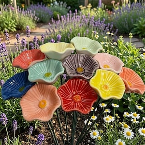 Può includere: Una collezione di dodici sculture di fiori in ceramica su sottili steli metallici, ognuna caratterizzata da un colore lucido unico tra cui rosso, giallo, blu, rosa e verde, con petali strutturati che si irradiano da uno stame centrale rialzato.
