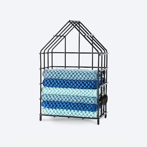 May include: A black metal house-shaped storage basket filled with six rolled, textured towels in shades of blue. The towels are stacked neatly inside the wireframe structure. A small black tag is attached to the side.