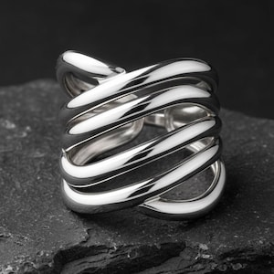 May include: A polished silver ring featuring a multi-layered, spiralling design with several interconnected bands that wrap around the finger. The metal surface is smooth and reflective, creating a continuous, flowing shape with open spaces.