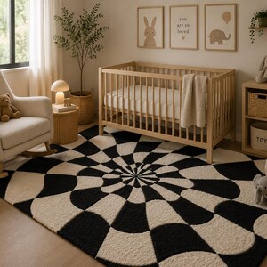 May include: A rectangular area rug featuring a high-contrast black and cream geometric pattern with a central radial design. The rug has a textured, tufted surface and covers the floor space in front of a wooden crib and a beige rocking chair.