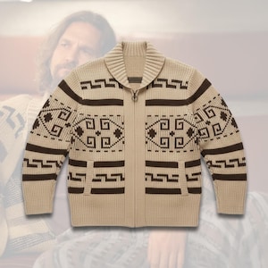 Può includere: Un cardigan beige con zip, collo a scialle e motivi geometrici marroni. Il maglione ha due tasche anteriori e una cerniera completa. Il design presenta forme geometriche ripetute in marrone su sfondo beige.