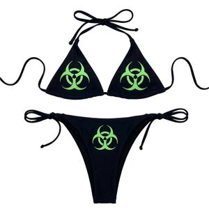 May include: Black bikini set with a biohazard symbol in neon green. The top is a triangle style with tie closures, and the bottom is a classic cut with side ties. The biohazard symbol is centered on both the top and bottom.