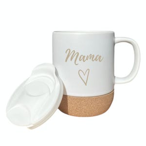 Puede incluir: Taza de cer&aacute;mica blanca con la palabra "Mama" en letras doradas y un s&iacute;mbolo de coraz&oacute;n. La parte inferior de la taza es de corcho. Una tapa blanca est&aacute; al lado de la taza.