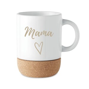 Puede incluir: Taza de cer&aacute;mica blanca con la palabra "Mama" en fuente dorada y un coraz&oacute;n dorado. La parte inferior de la taza es de corcho. La taza tiene un asa curvada.