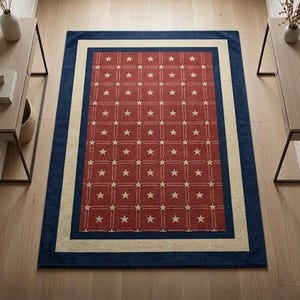 May include: Rectangular area rug with a patriotic theme. The rug features a red center with a grid of white stars. It is bordered by a cream-colored stripe and a navy blue edge. The rug is placed on a light wood floor.