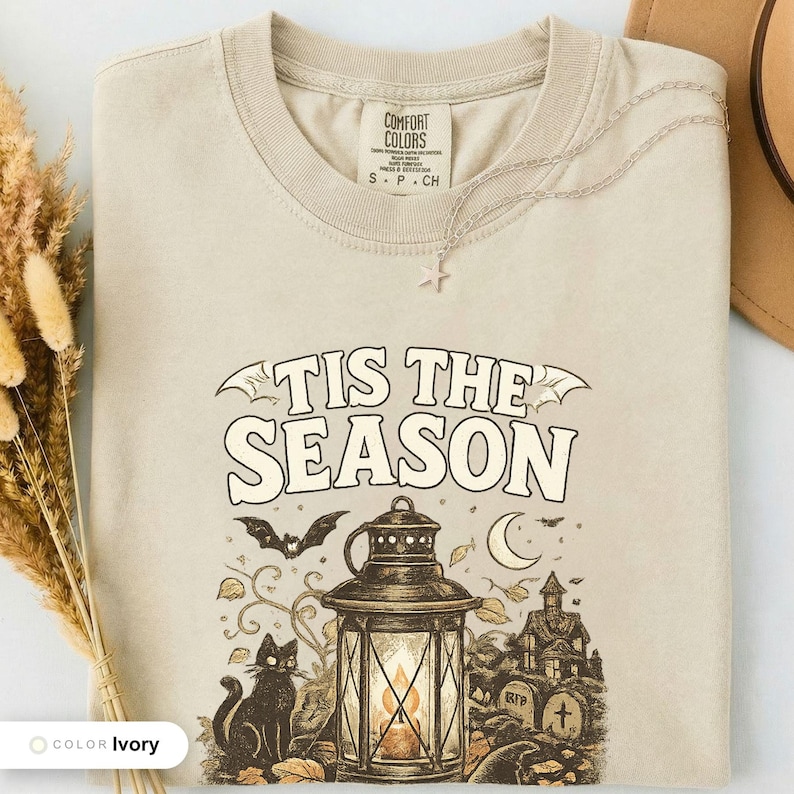 Ivory shirt folded flat and photographed from above, printed with "Haunted Harvest Lantern" across the chest.