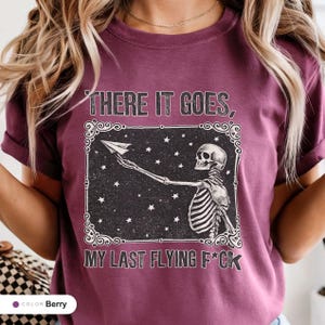 Model wearing a berry t-shirt printed with "Last Nerve Bat-Free Skeleton" across the chest.