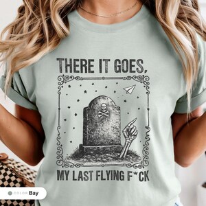 Model wearing a bay t-shirt printed with "Last Flying F*ck in the Graveyard" across the chest.