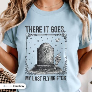 Model wearing a chambray t-shirt printed with "Last Flying F*ck in the Graveyard" across the chest.