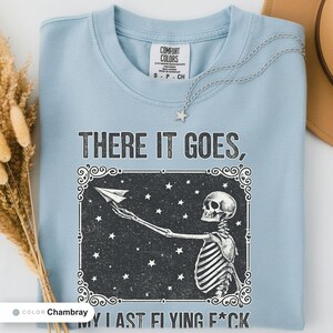 Chambray t-shirt folded flat and photographed from above, printed with "Last Nerve Bat-Free Skeleton" across the chest.