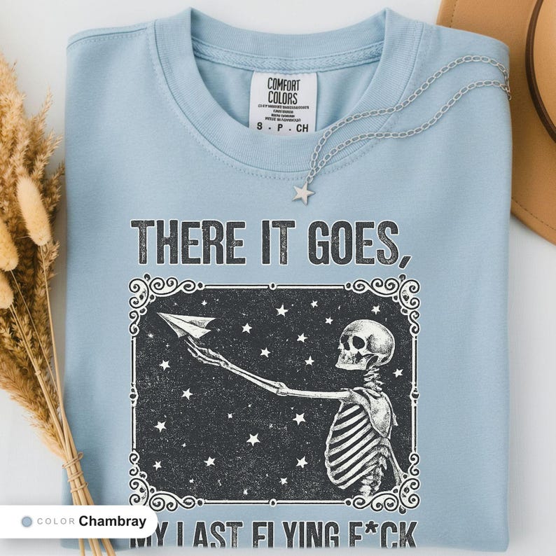 Chambray t-shirt folded flat and photographed from above, printed with "Last Nerve Bat-Free Skeleton" across the chest.