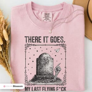 Blossom t-shirt folded flat and photographed from above, printed with "Last Flying F*ck in the Graveyard" across the chest.