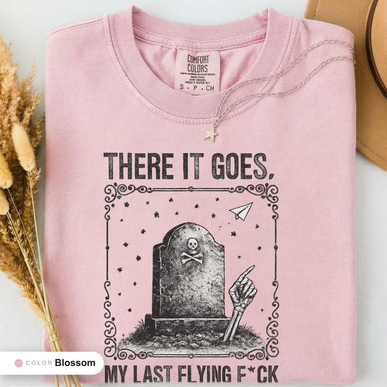 Blossom t-shirt folded flat and photographed from above, printed with "Last Flying F*ck in the Graveyard" across the chest.