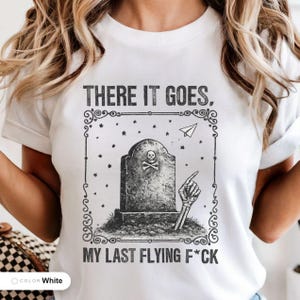 Model wearing a white t-shirt printed with "Last Flying F*ck in the Graveyard" across the chest.