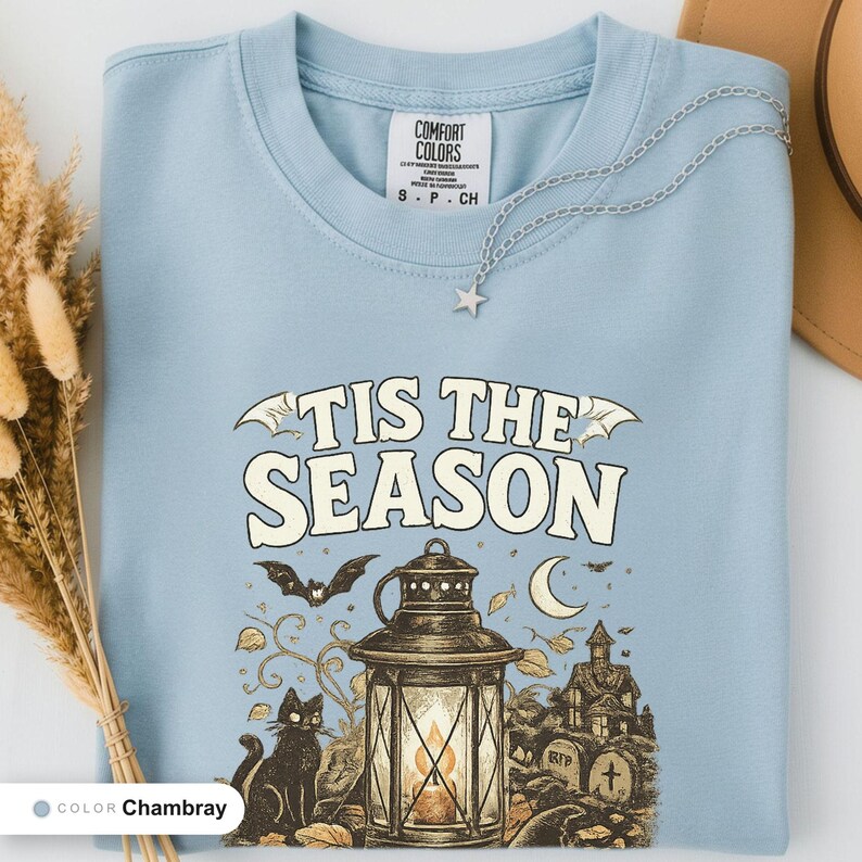 Chambray shirt folded flat and photographed from above, printed with "Haunted Harvest Lantern" across the chest.
