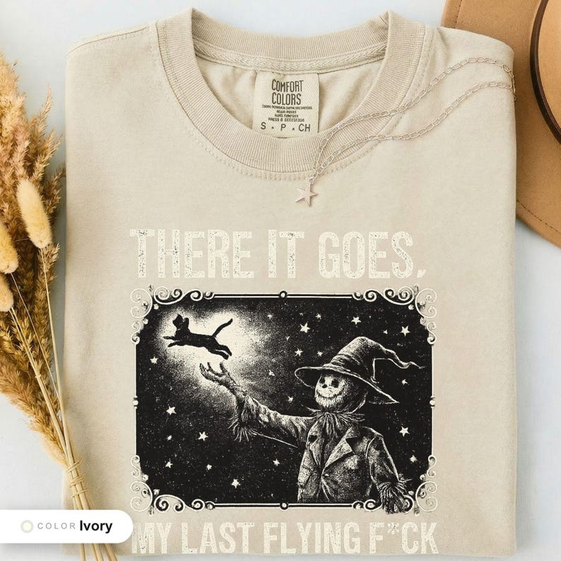 Ivory t-shirt folded flat and photographed from above, printed with "Last Flight Skeleton Bat" across the chest.