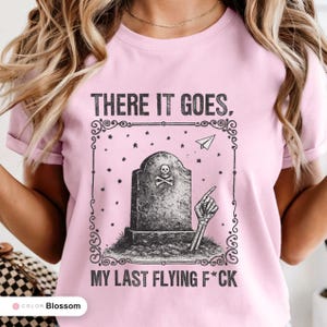Model wearing a blossom t-shirt printed with "Last Flying F*ck in the Graveyard" across the chest.