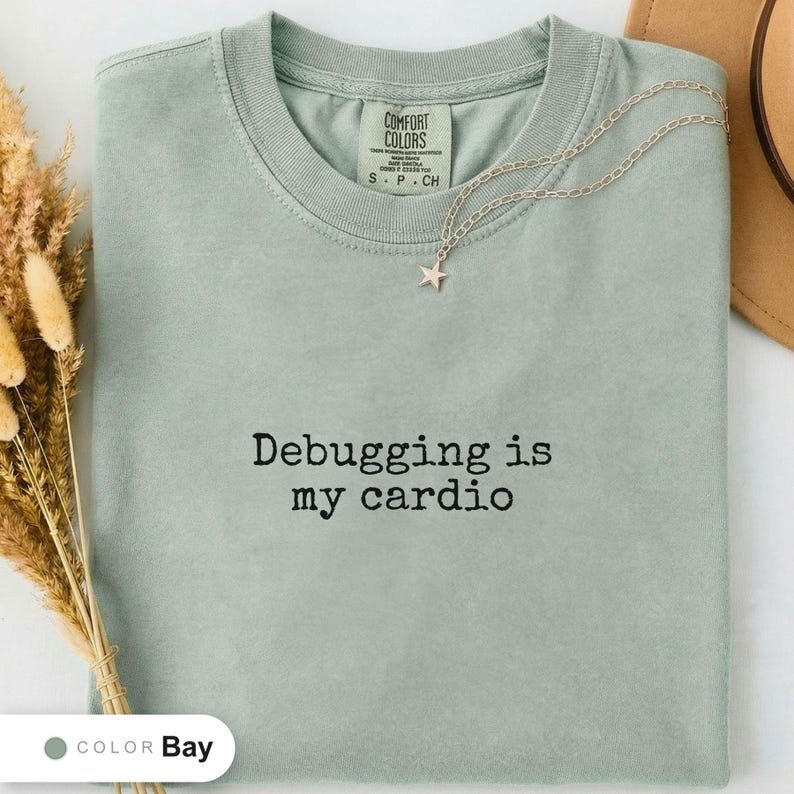 Bay t-shirt folded flat and photographed from above, printed with "Debugging is my cardio" across the chest.