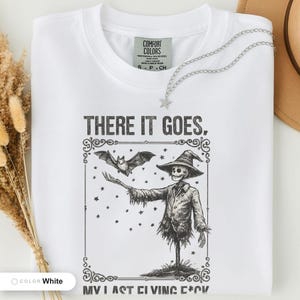 White t-shirt folded flat and photographed from above, printed with "Graveyard Bat Catcher" across the chest.