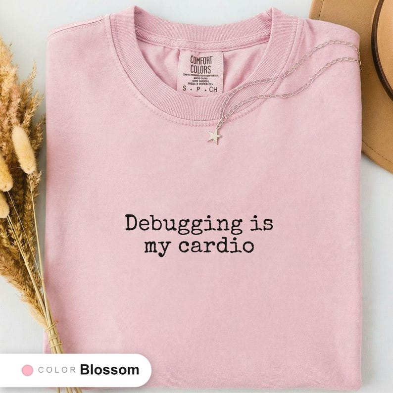 Blossom t-shirt folded flat and photographed from above, printed with "Debugging is my cardio" across the chest.