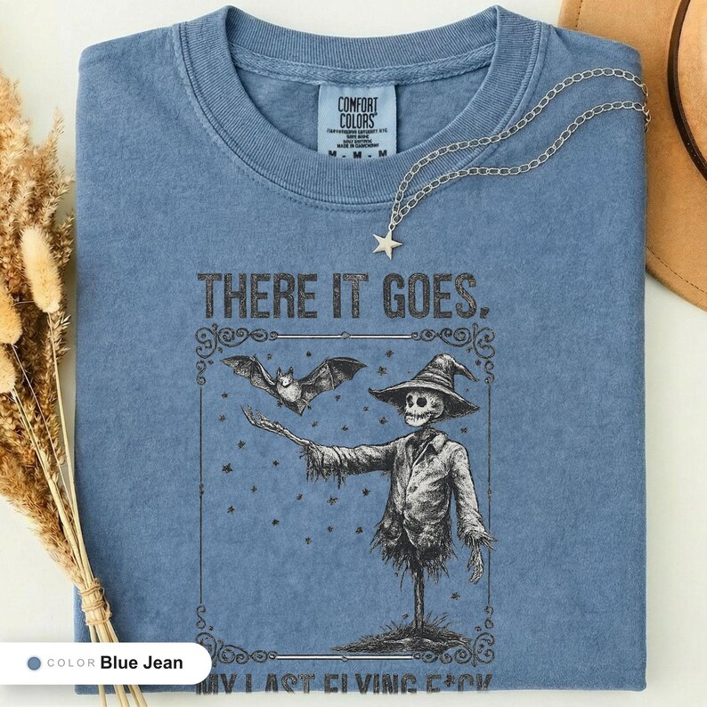 Blue jean t-shirt folded flat and photographed from above, printed with "Graveyard Bat Catcher" across the chest.