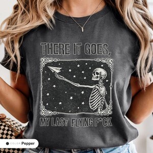 Model wearing a pepper t-shirt printed with "Last Nerve Bat-Free Skeleton" across the chest.