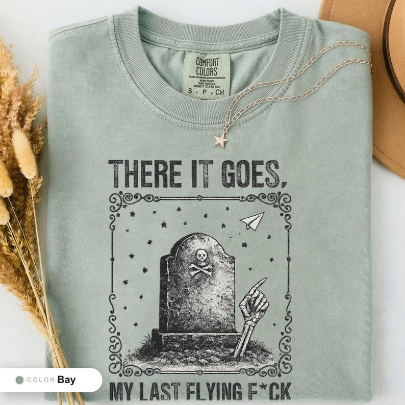 Bay t-shirt folded flat and photographed from above, printed with "Last Flying F*ck in the Graveyard" across the chest.