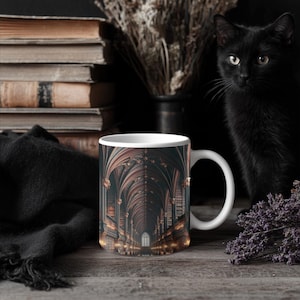 May include: White ceramic mug featuring a detailed illustration of a gothic library interior. A black cat sits nearby. The mug is on a wooden surface with books and dried flowers in the background.