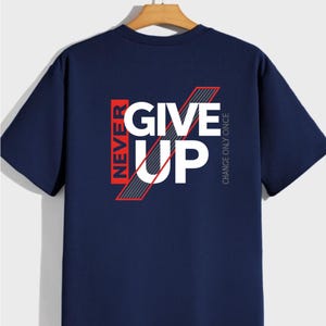 May include: Navy blue t-shirt with the words "NEVER GIVE UP" in white and red block letters. The shirt has a ribbed texture and short sleeves. The phrase "CHANCE ONLY ONCE" is printed vertically on the right side.