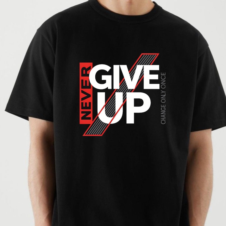 May include: Black t-shirt with the words "NEVER GIVE UP" in white and red block letters. The phrase "CHANGE ONLY ONCE" is printed vertically on the right side of the shirt. The shirt is made of a soft material.