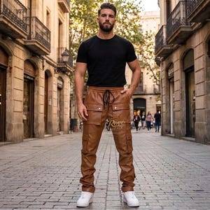 May include: Brown leather cargo pants with multiple pockets and a drawstring waist. The pants have a relaxed fit and are paired with a black t-shirt and white sneakers. The pants have the text "Rovo Leather" printed on them.