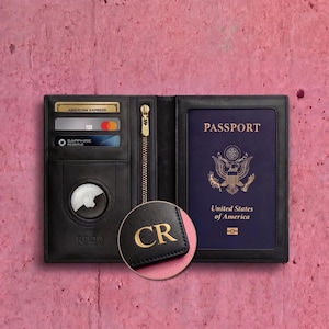May include: Black leather passport wallet with a gold zipper, credit card slots, and a clear window for a passport. The wallet has a gold embossed "CR" on a small leather tag. The passport reads "Passport" and "United States of America."