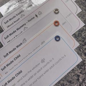 Może przedstawiać: Stos białych kart z zaokrąglonymi rogami i kolorowymi oczkami. Tekst na kartach zawiera "Soft Mode" oraz słowa takie jak "Daddy", "Mummy", "Work" i "Child". Karty zawierają również instrukcje i ikonę uśmiechniętej buzi.