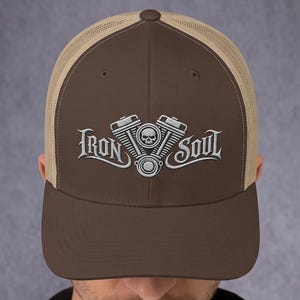 Könnte beinhalten: Eine braune Trucker-Cap mit beigem Netzrücken und einfarbiger brauner Vorderseite. Auf der Vorderseite befindet sich eine weiße Stickerei eines V-Twin-Motors mit einem Totenkopf in der Mitte, flankiert vom Schriftzug Iron Soul in gotischer Schrift.