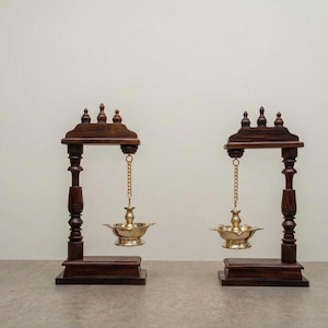 Peut inclure: Deux supports en bois brun foncé, chacun doté d'un pilier vertical et d'une pièce supérieure horizontale avec trois petits fleurons. Une lampe à huile en métal doré est suspendue au centre de chaque pièce supérieure par une courte chaîne.