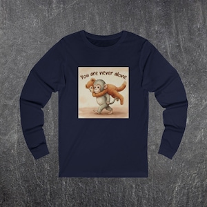 Puede incluir: Camiseta de manga larga azul marino con una ilustración en acuarela de dos monos, uno cargando al otro. La imagen incluye el texto "You are never alone" en una fuente manuscrita. La camiseta es de material suave.