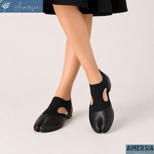 Op de afbeelding: Zwarte schoenen met split-teen en een uniek ontwerp. De schoenen hebben een zwarte leren teenpartij en een zwart stoffen bovenwerk met een uitgesneden detail. De schoenen zijn ontworpen met een split-teen, een stijlvolle schoenoptie.