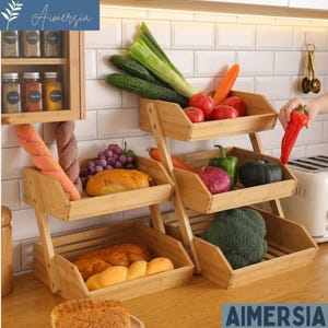 May include: A three-tiered bamboo produce stand filled with fresh vegetables, fruits, and bread. The stand holds tomatoes, cucumbers, carrots, grapes, and a red bell pepper. Breads and a loaf of bread are also displayed. The stand is on a wooden countertop.